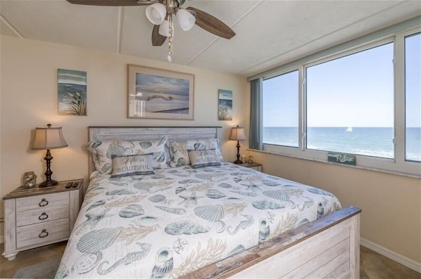 Ein Schlafzimmer mit einem großen Bett, einem Deckenventilator und Meerblick durch ein Fenster.