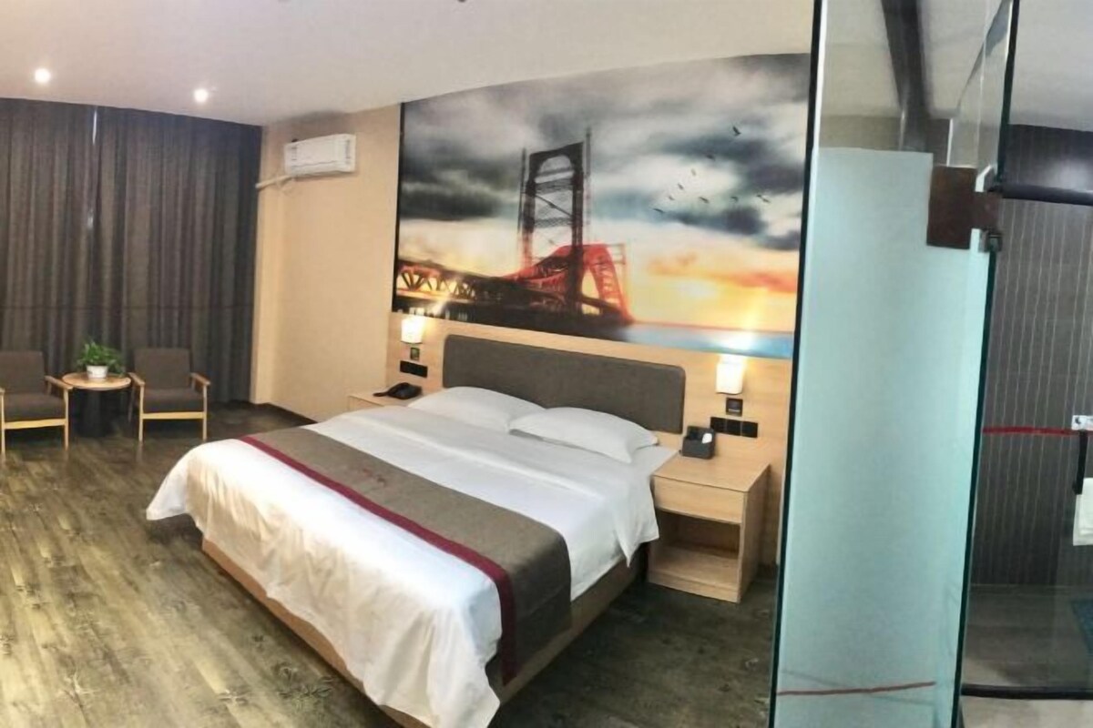 A hotel room with a bed, bedside tables, a chair, a desk, and a glass partition.