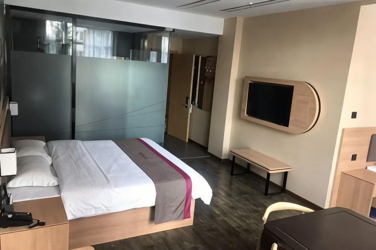 A hotel room with a bed, bedside table, TV, and a desk.
