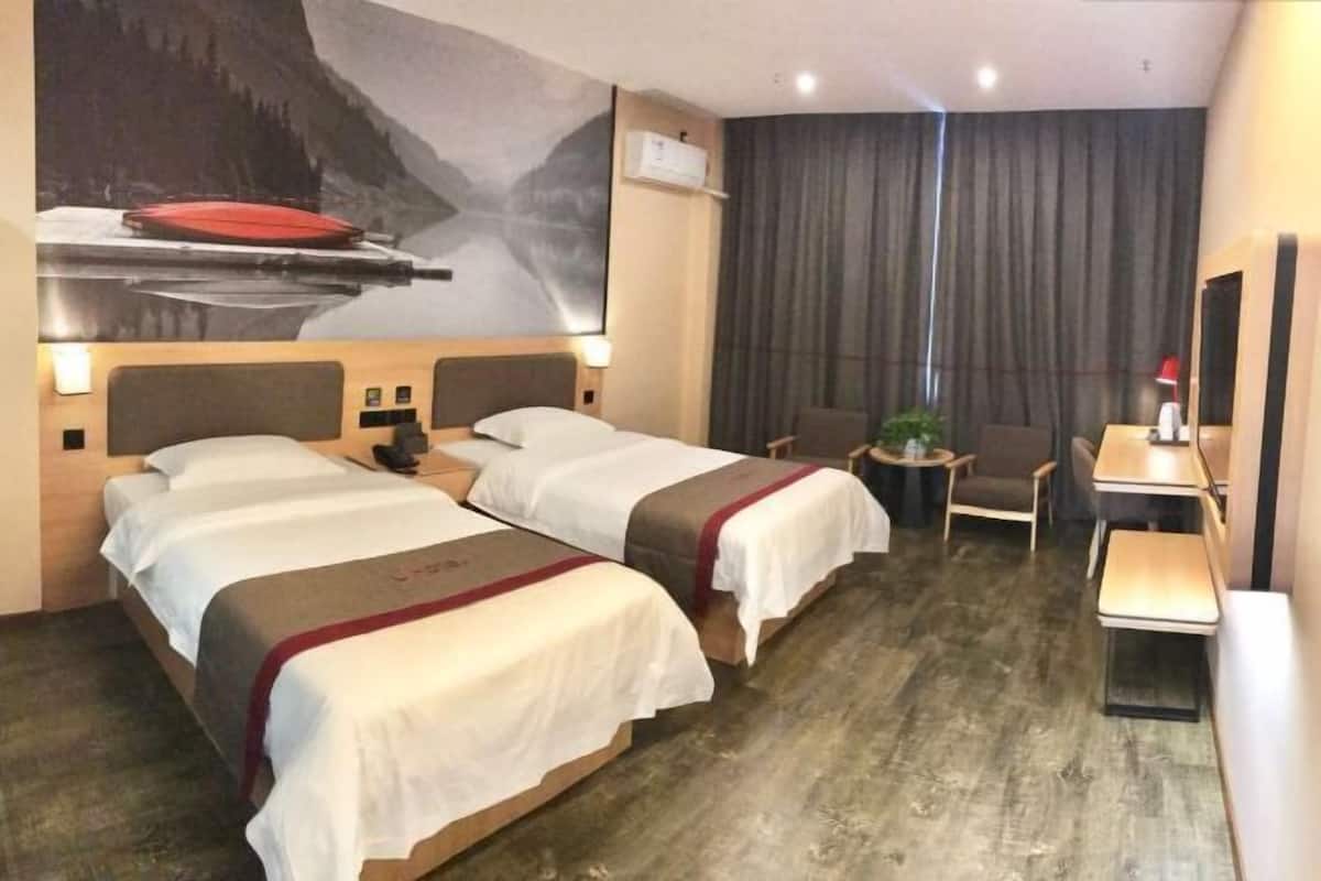 Ein Hotelzimmer mit zwei Betten, einem Schreibtisch, einem Stuhl, einem kleinen Tisch und einem großen Fenster mit Vorhängen.
