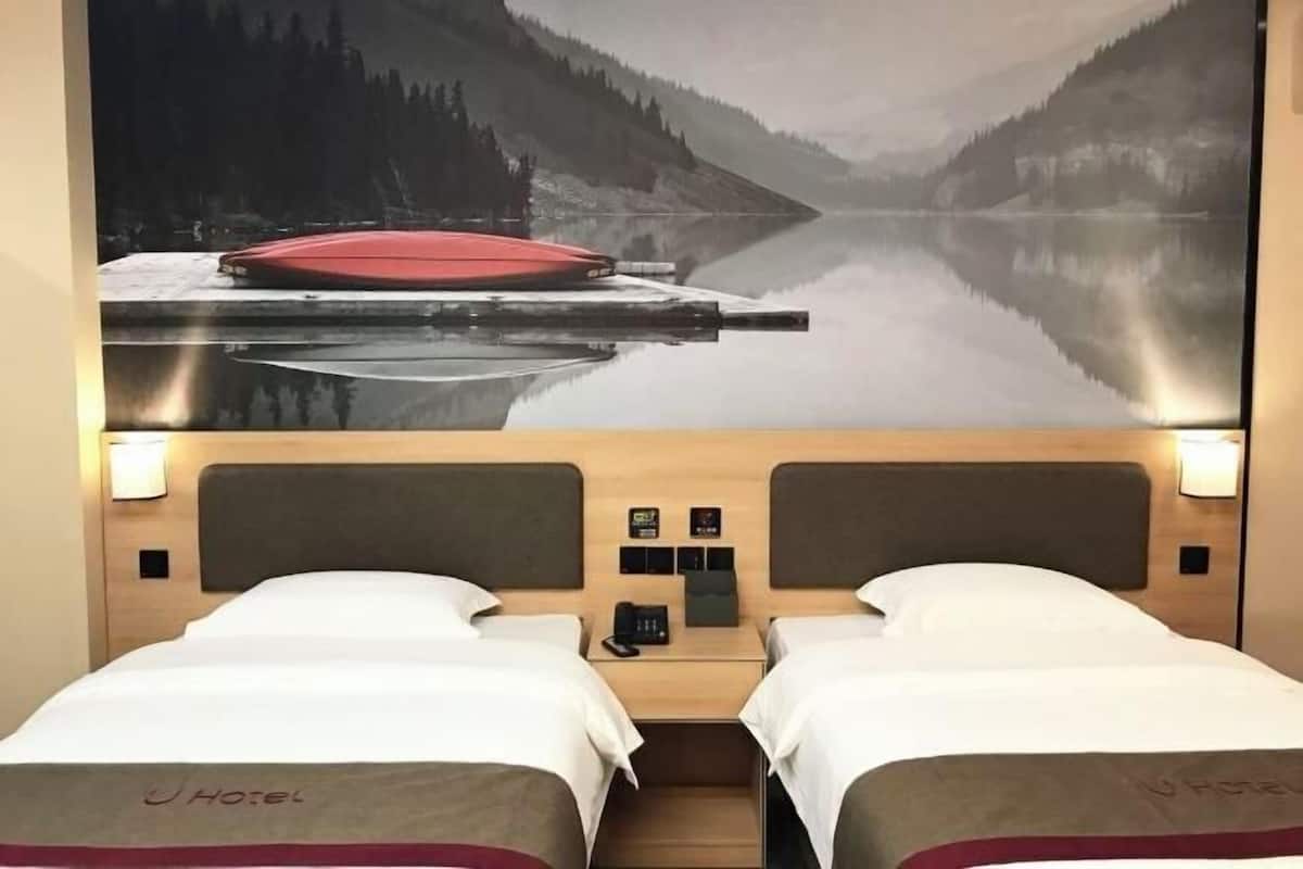 Ein Hotelzimmer mit zwei Betten, einem hölzernen Kopfteil, einem Nachttisch mit Telefon und einem an der Wand montierten Fernseher, der eine Seeblick zeigt.