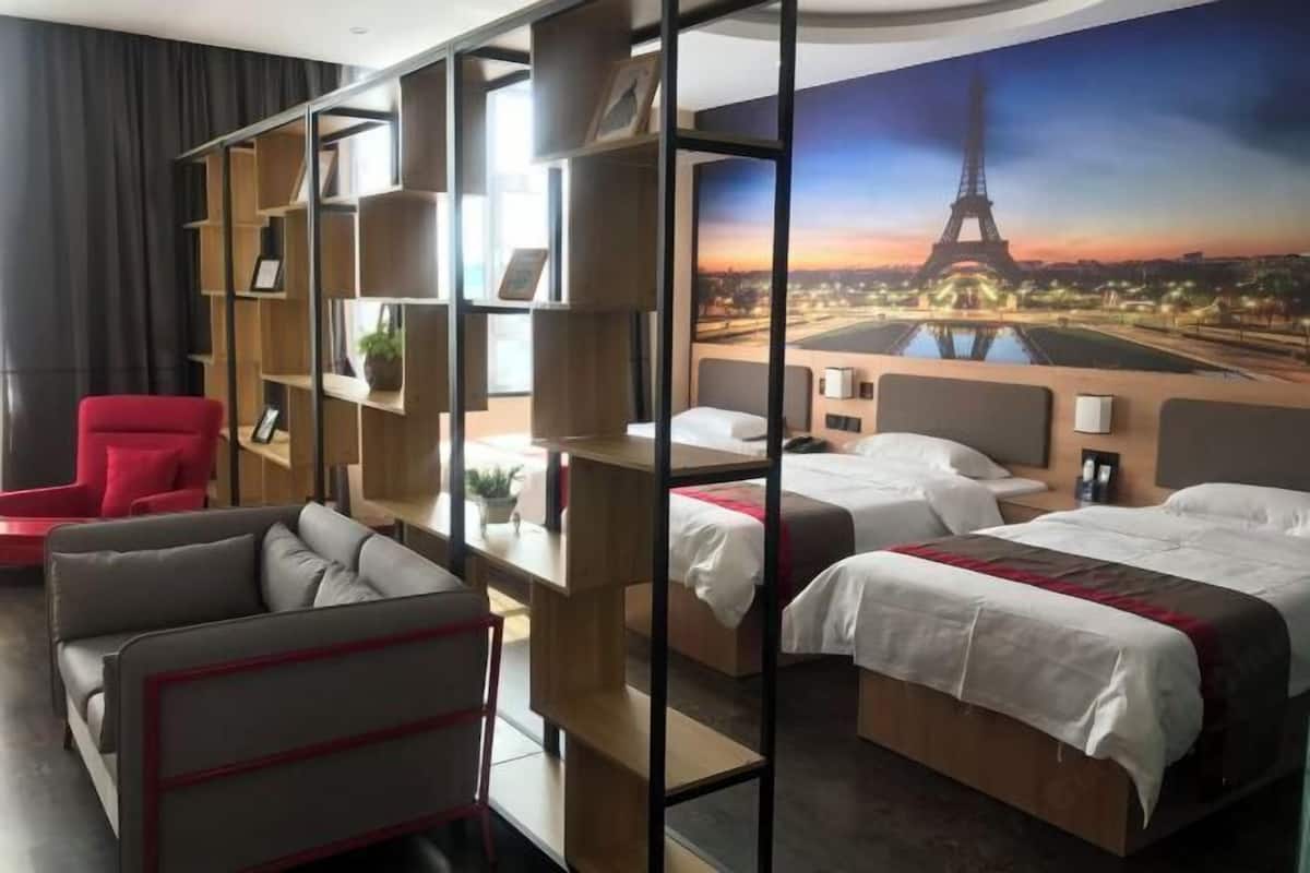 Ein Hotelzimmer mit einem großen Bett, einem roten Sessel, einer Couch und einem Bücherregal.