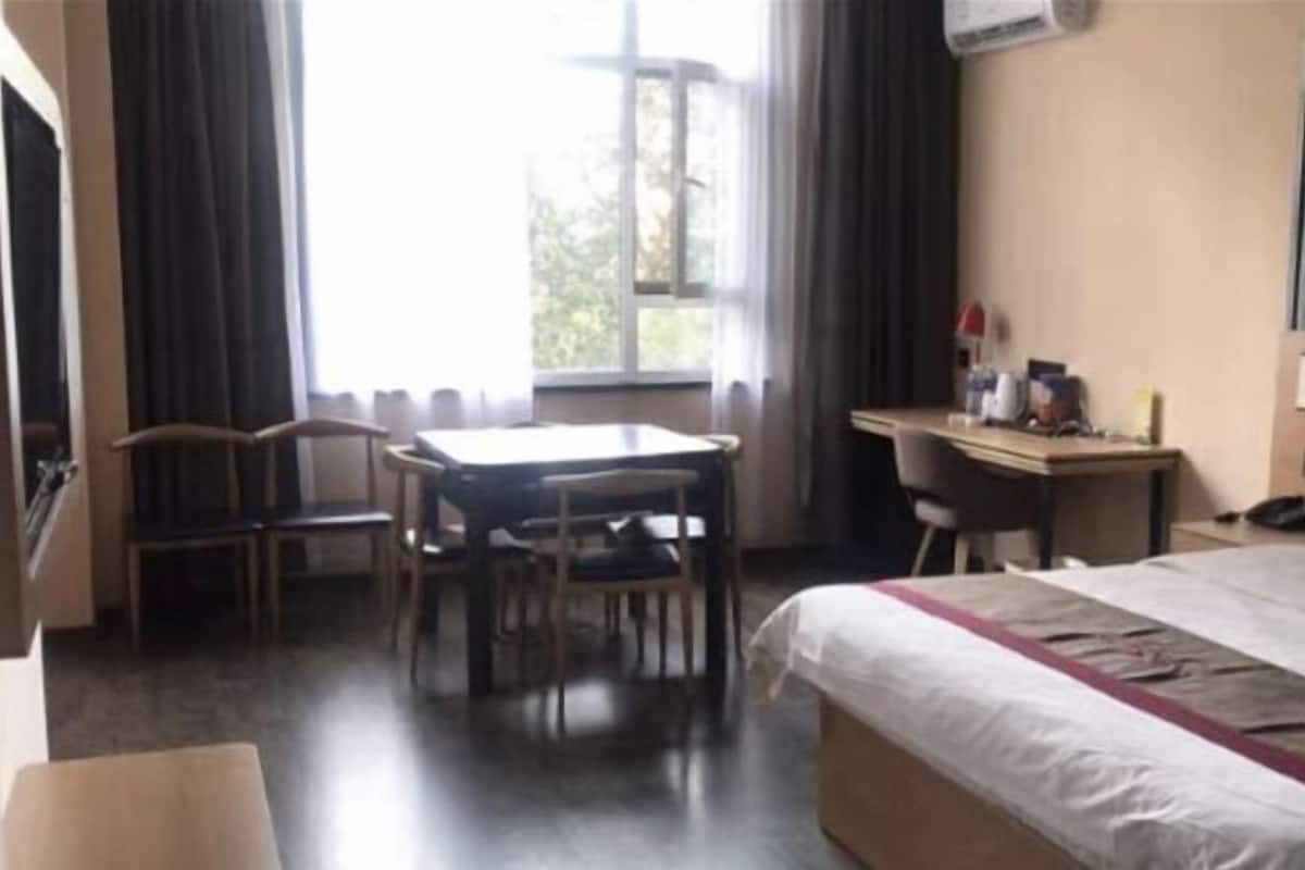 Ein Hotelzimmer mit Bett, Schreibtisch, zwei Stühlen und einem fensterbepflanzten Fenster.