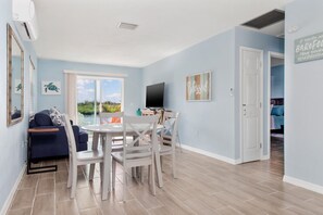 Relax in this serene space with a view of lush greenery, featuring a flat-screen TV, dining table, and comfortable sofa.