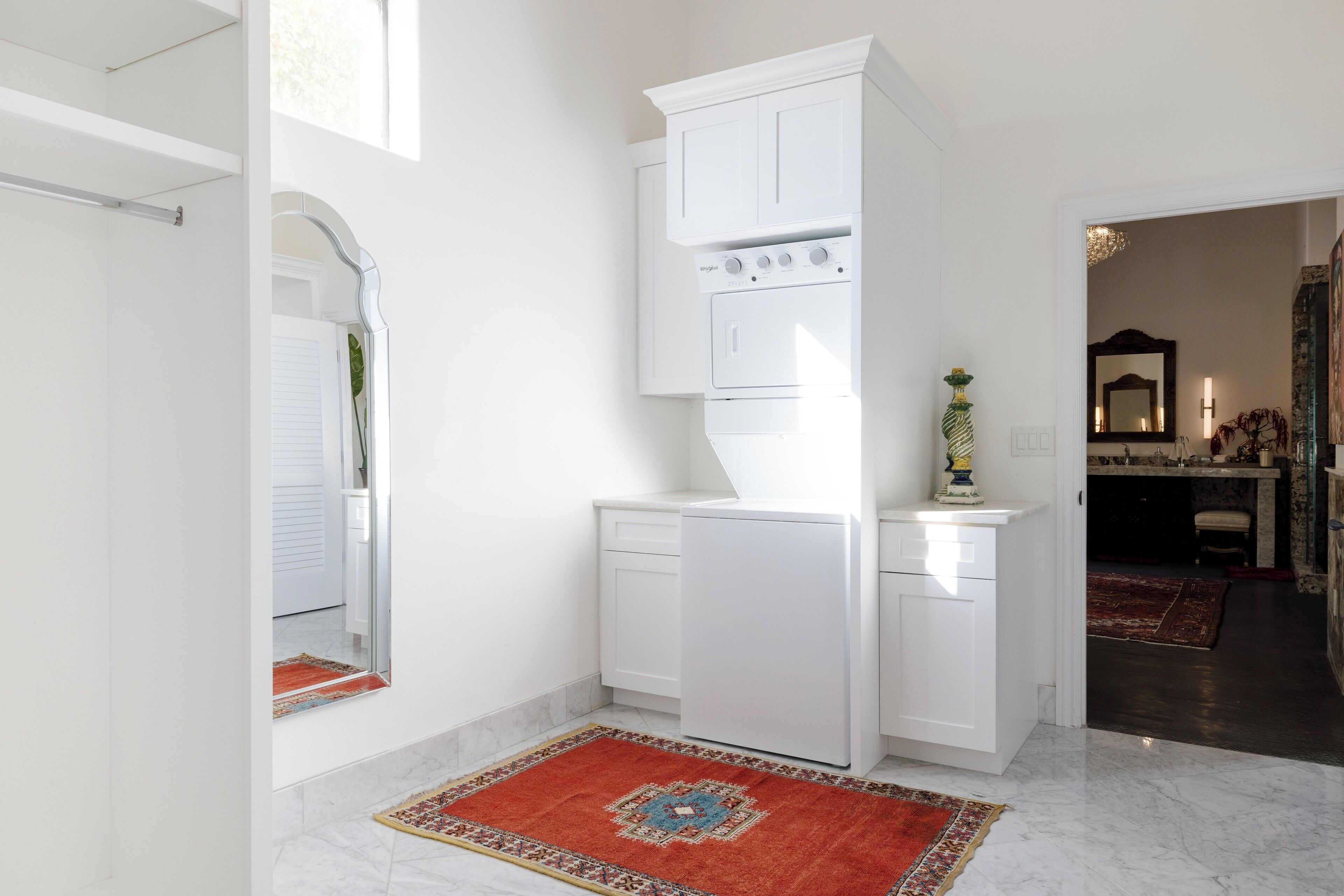 Une cuisine de taille réduite avec des meubles blancs, un four encastré et un tapis rouge à motifs.