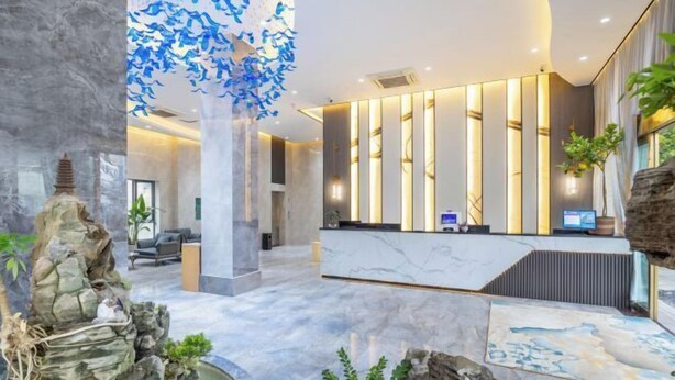 A modern lobby with a reception desk, seating area, and a decorative rock feature. - Guangyi Hotel (Quanzhou)