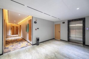 A hotel corridor with a marble floor, a trash bin, and an elevator. - Guangyi Hotel (Quanzhou)