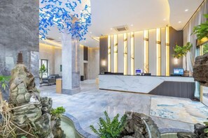 A modern hotel lobby with a reception desk, seating area, and decorative elements like a rock formation and a tree with blue leaves. - Guangyi Hotel (Quanzhou)