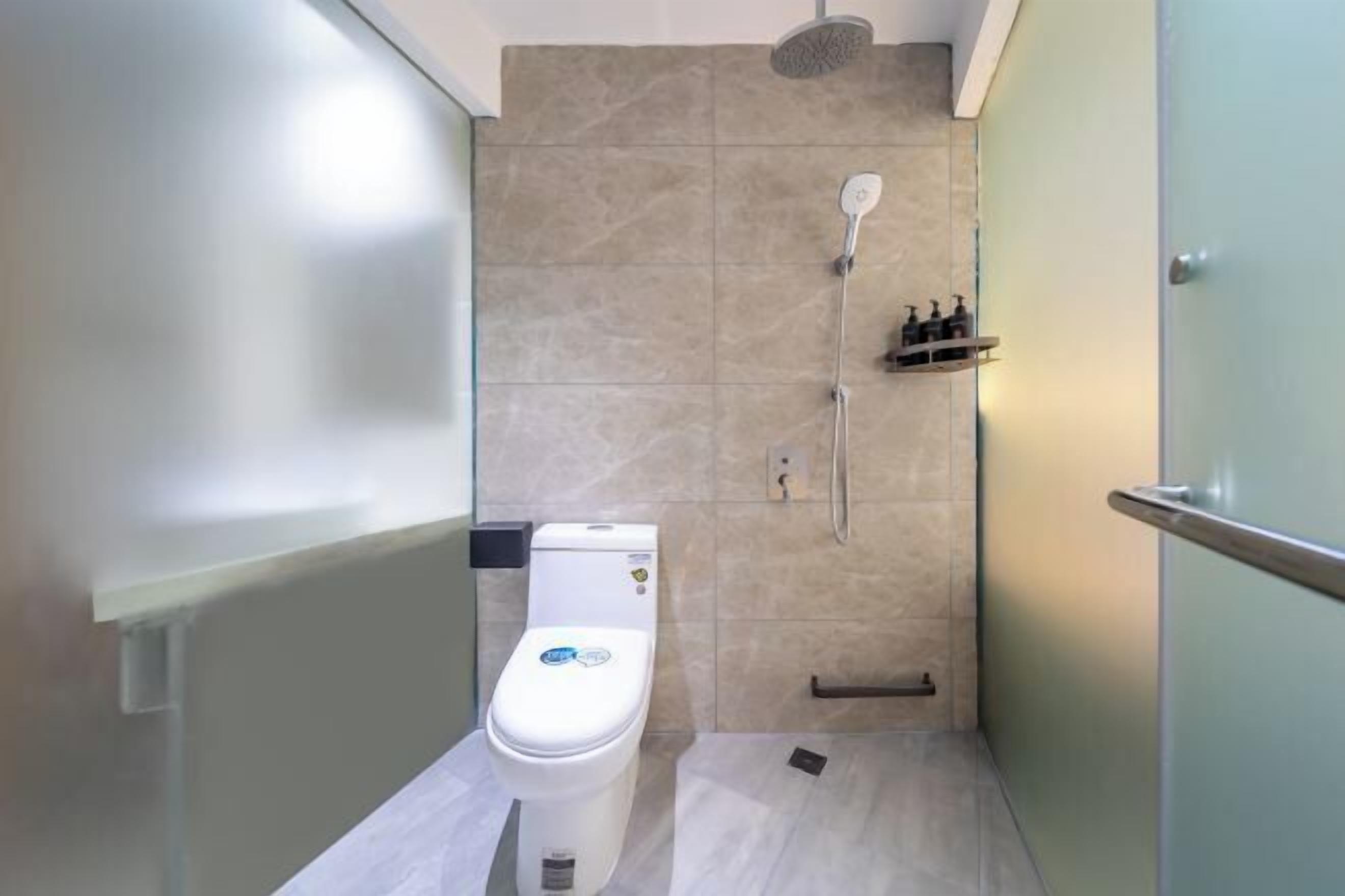 A modern bathroom with a toilet, shower, and a small shelf with toiletries.