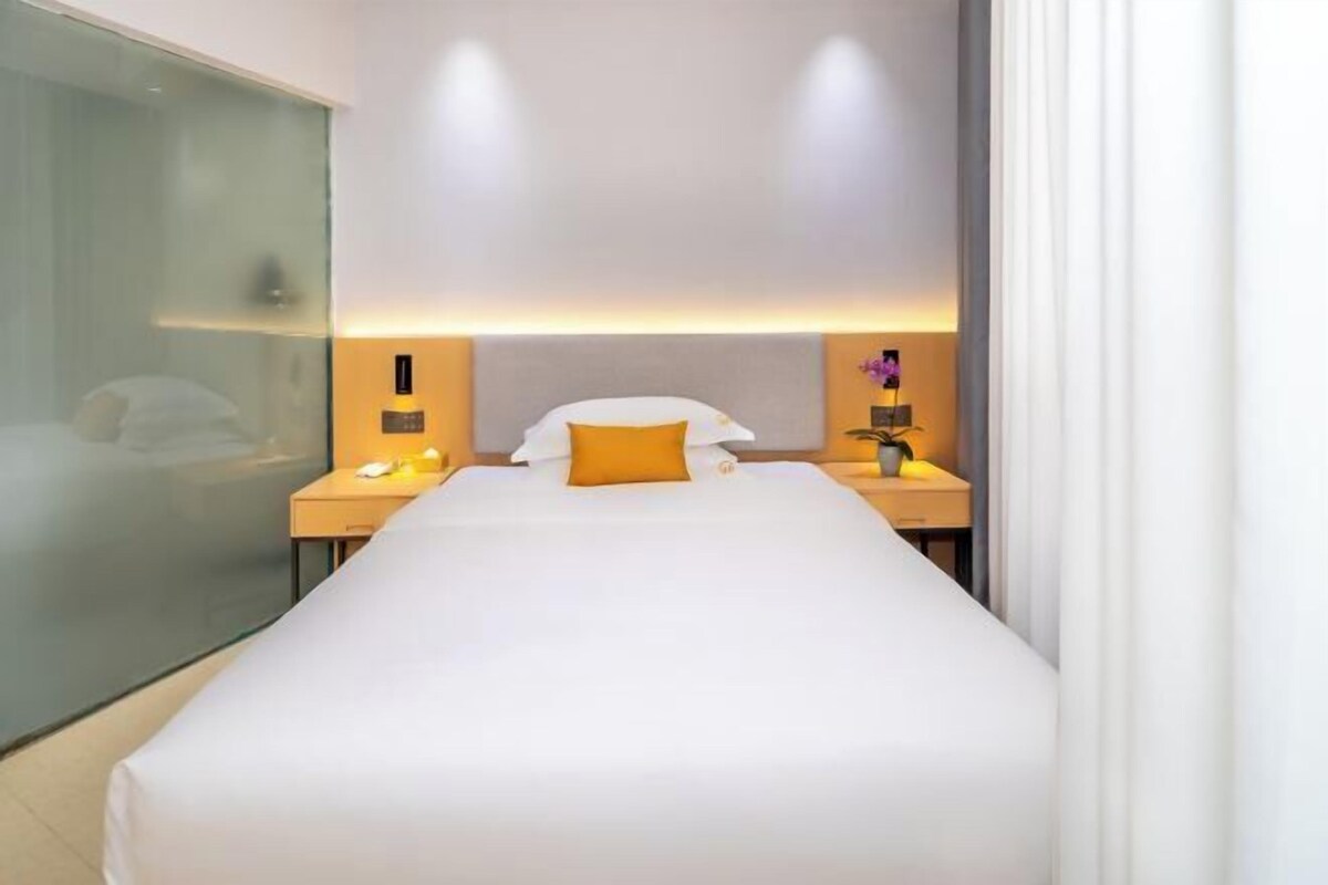 A hotel room with a large bed, a bedside table with a lamp, and a glass partition wall.