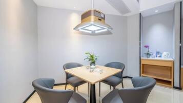 Un comedor moderno con una mesa cuadrada y cuatro sillas, una lámpara colgante y una planta pequeña sobre la mesa.
