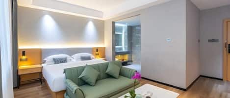 A modern hotel room with a bed, a green sofa, a white coffee table, and a large window.
