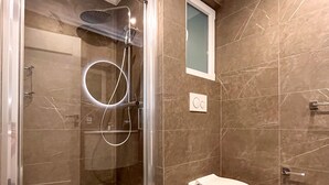 Un baño moderno con ducha envuelta en vidrio, un inodoro y suelo de mármol.