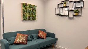 Un sofá color turquesa con cojines estampados, un expositor de suculentas de madera montado en la pared y estanterías geométricas negras con plantas.