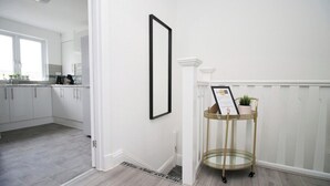 A hallway with a white door, a framed picture, and a gold wire shelf with a plant. - Albany House by Tŷ SA (Cardiff)