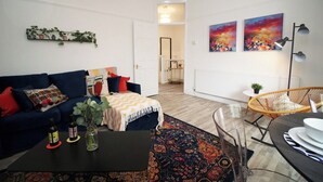 A modern living room with a blue sofa, a coffee table, and a wicker chair. There are two paintings on the wall and a radiator. - Albany House by Tŷ SA (Cardiff)