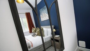 A bedroom with a bed, bedside table, lamp, and a window with curtains. - Albany House by Tŷ SA (Cardiff)