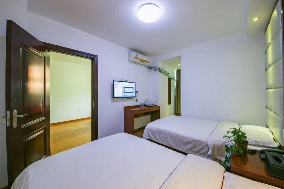 A hotel room with two beds, a desk with a computer, a mirror, and a plant.