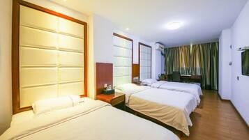 Quarto de hotel com três camas, uma cabeceira de madeira, televisão e janela com cortinas.