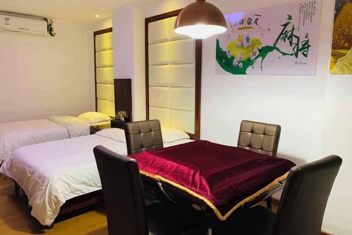 A hotel room with two beds, a dining table with chairs, a pendant light, and a wall with artwork.