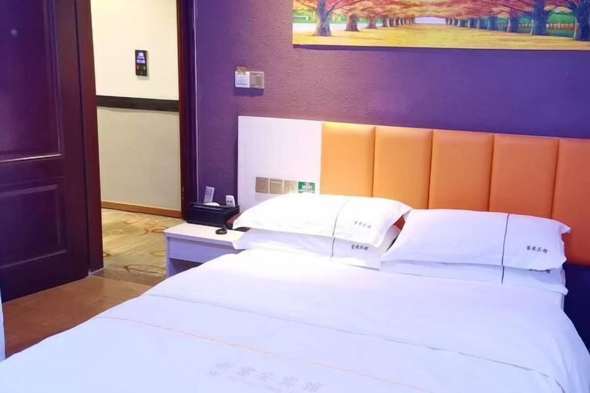 A hotel room with a bed, a nightstand, a painting on the wall, and a door.