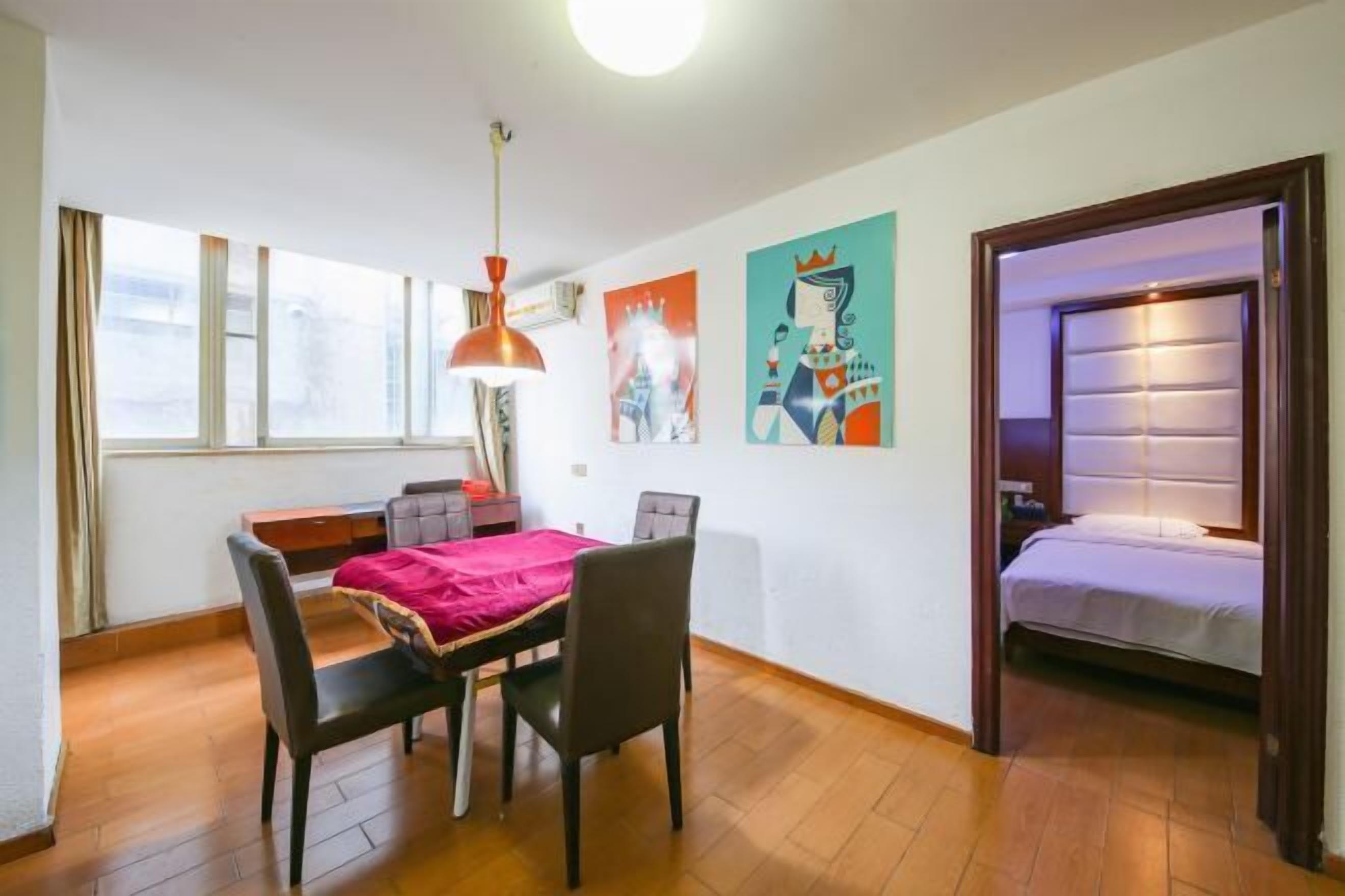 A room with a dining table, chairs, a bed, and artwork on the walls.