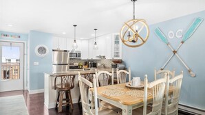 Una cucina moderna con mobili bianchi, elettrodomestici in acciaio inossidabile e zona pranzo con tavolo in legno e sedie bianche.