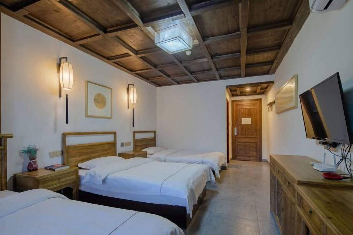 Een hotelkamer met drie enkele bedden, houten hoofdborden en een televisie op een houten dressoir.
