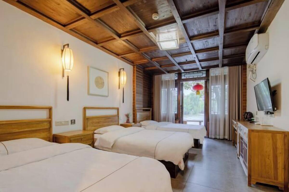 Een hotelkamer met houten balken in het plafond, drie bedden, een houten bureau, een televisie en een raam met gordijnen.