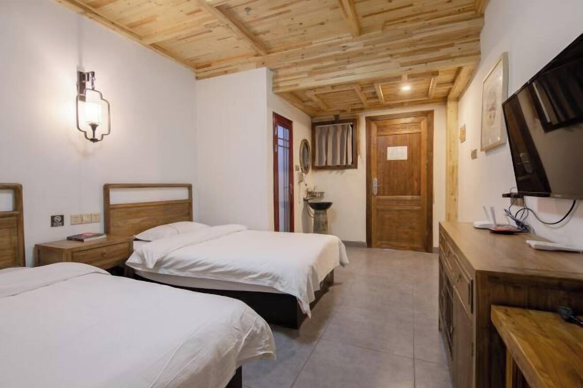 Een hotelkamer met twee bedden, een houten plafond, een televisie en een bureau met een computer.