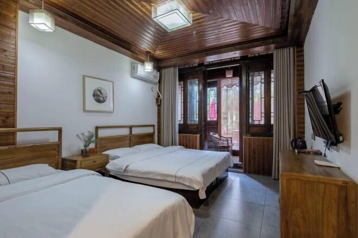 Een kamer met twee bedden, een houten plafond, een televisie en een deur naar buiten.