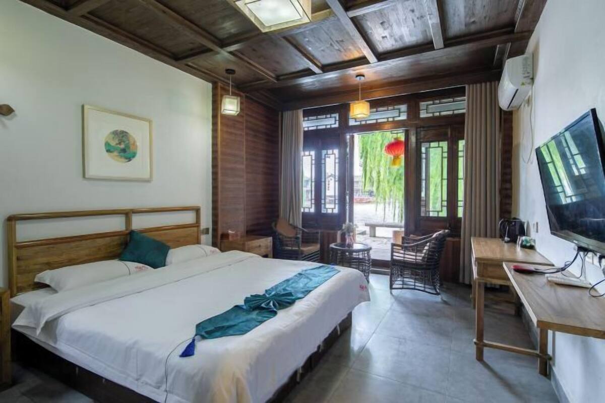 Een hotelkamer met een groot bed, een bureau met een televisie, een klein tafeltje en stoelen.