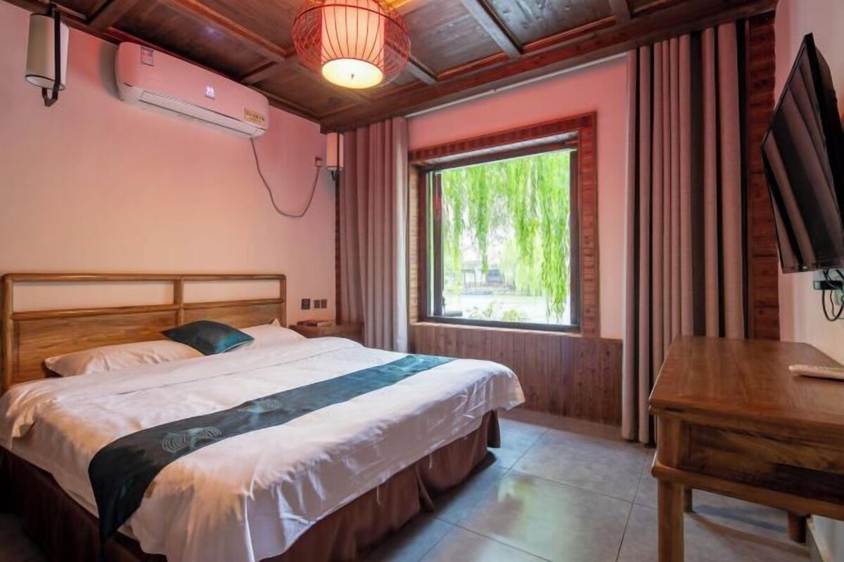 Een slaapkamer met een bed, een houten hoofdbord, een raam met gordijnen, een televisie en een airconditioning.