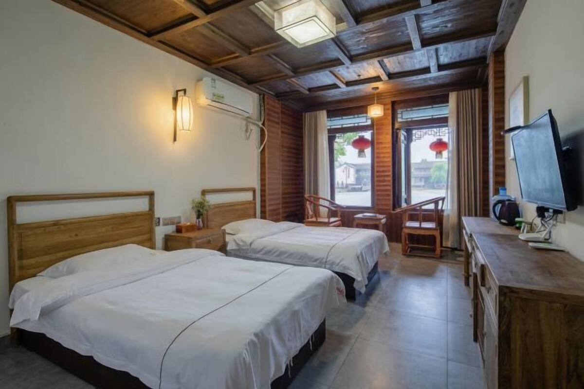 Een hotelkamer met twee bedden, een houten bureau, een televisie en een raam met uitzicht op het omliggende landschap.