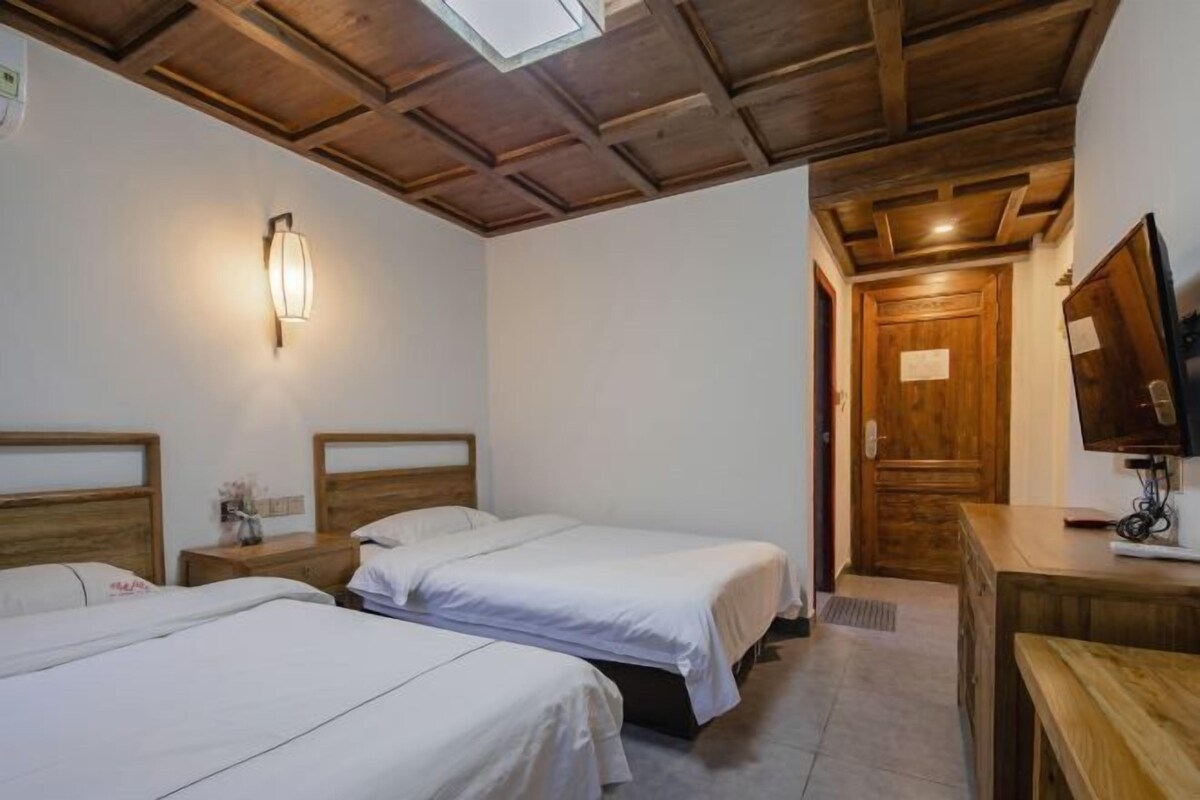 Een kamer met twee bedden, houten hoofdborden, een aan de muur bevestigde lamp, een houten deur en een bureau met een televisie.