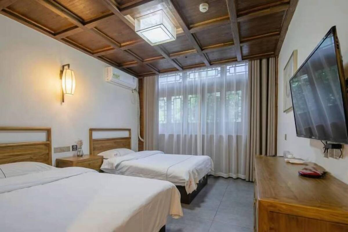 Hotelkamer met twee eenpersoonsbedden, een houten bureau met een televisie, een wandairconditioner en een raam met dunne gordijnen.