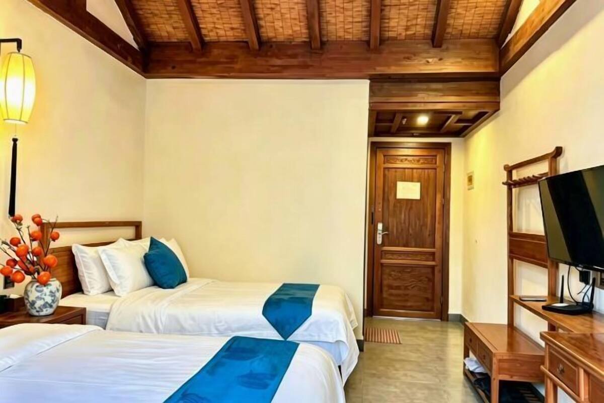 Een hotelkamer met twee bedden, een houten plafond, een televisie en een deur naar een andere kamer.