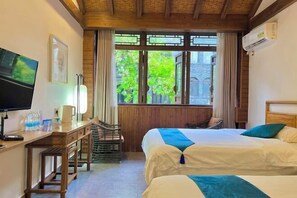 Een hotelkamer met een houten bureau, twee bedden, een televisie en een raam met uitzicht op groen.