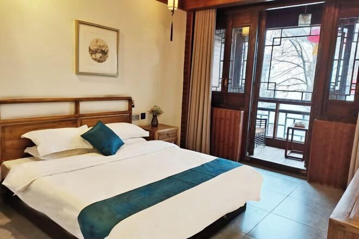 Een hotelkamer met een groot bed, een houten hoofdeinde, een ingelijste foto aan de muur en uitzicht door een glazen deur.