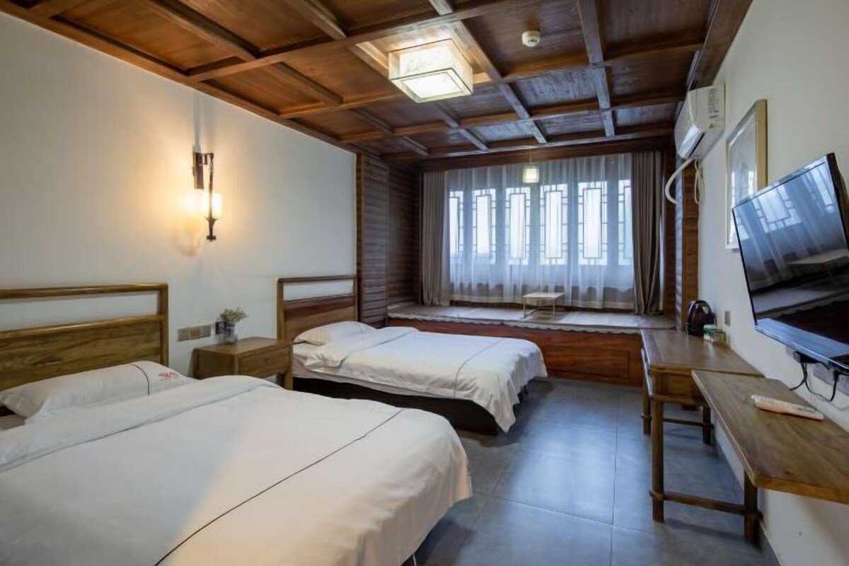 Een hotelkamer met twee eenpersoonsbedden, een houten bureau, een televisie en een raam met gordijnen.