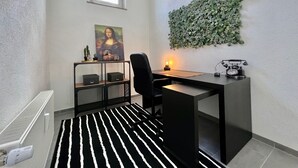 Un espacio de oficina moderno con un escritorio, una silla y un teléfono montado en la pared. Hay una ventana, un cuadro y un adorno verde en la pared.