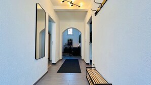 Un pasillo con un banco de madera, una alfombra negra y un candelabro en el techo.
