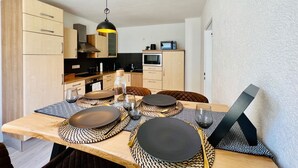Una cocina moderna con armarios de madera, una lámpara colgante negra y un comedor con platos negros y individuales de fibra.