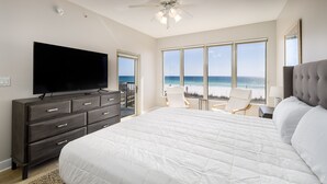 Quarto com uma cama grande, televisão, cadeira e vista para o mar.