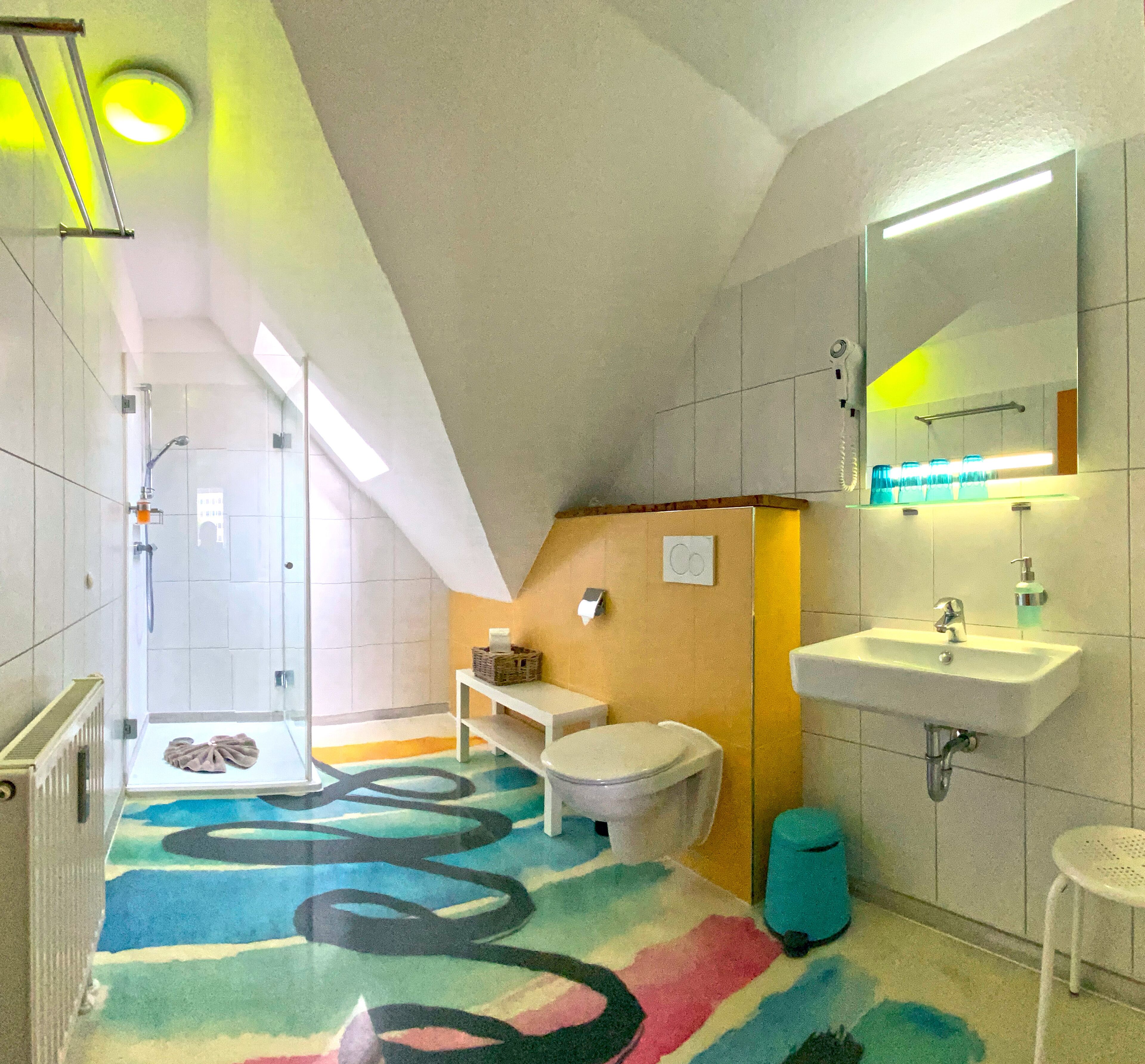 A modern bathroom with a shower, toilet, sink, and a colorful rug.
