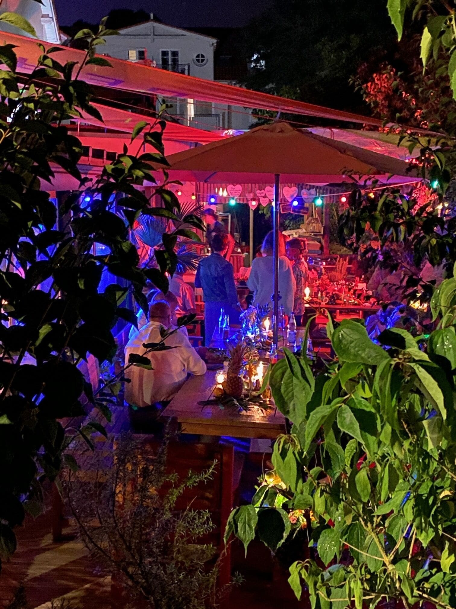 Un área de comedor al aire libre con mesas y sillas, rodeada de follaje.