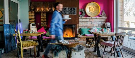 A cozy interior with a brick fireplace, wooden furniture, and a large window.