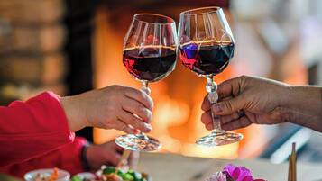 Dos personas brindando con copas de vino, una vela y un pequeño florero con flores sobre una mesa de madera.