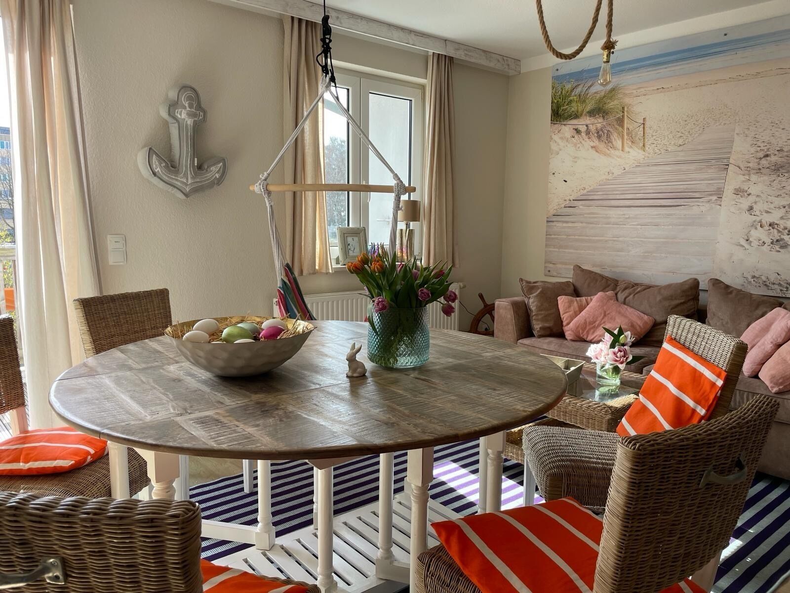 Un salon chaleureux avec une table ronde en bois, des meubles en osier et une fresque murale sur le thème de la plage.