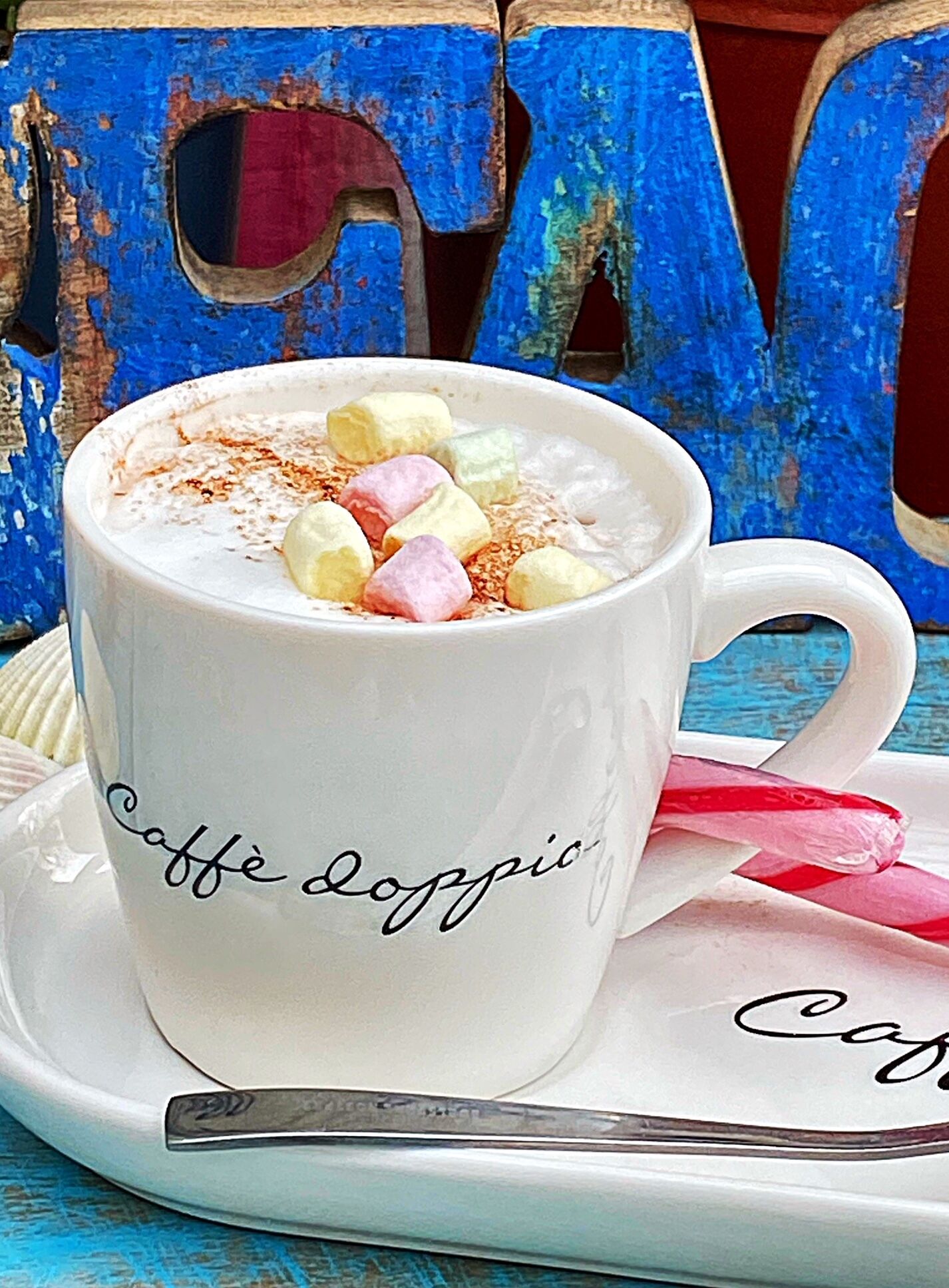 A white mug with "Caffe Loppio" written on it, filled with a frothy beverage and topped with colorful marshmallows and a sprinkle of cinnamon.